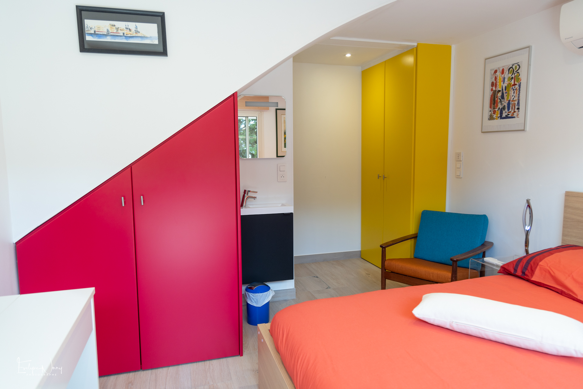 Photo n°2 de la Chambre principale de l'appartement en rez-de-jardin. Armoire et lave-mains et fauteuil en plus du lit et de la table et TV