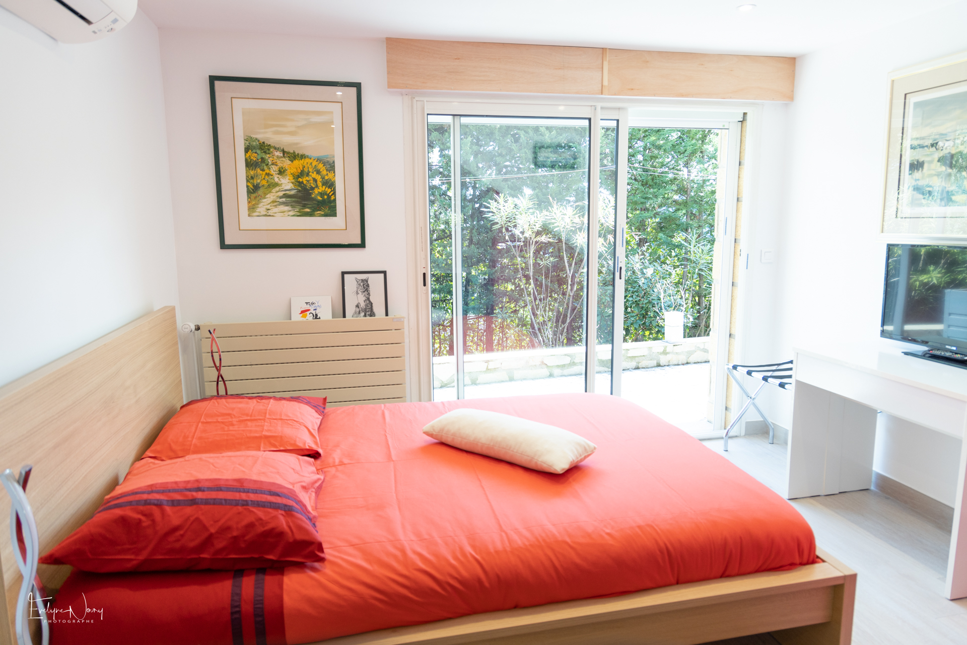 Photo de la chambre principale de l'appartement en rez-de-jardin. 1 lit double avec couette en 140cm. Baie vitrée avec accès au jardin. Table, télévision. Radiateur.