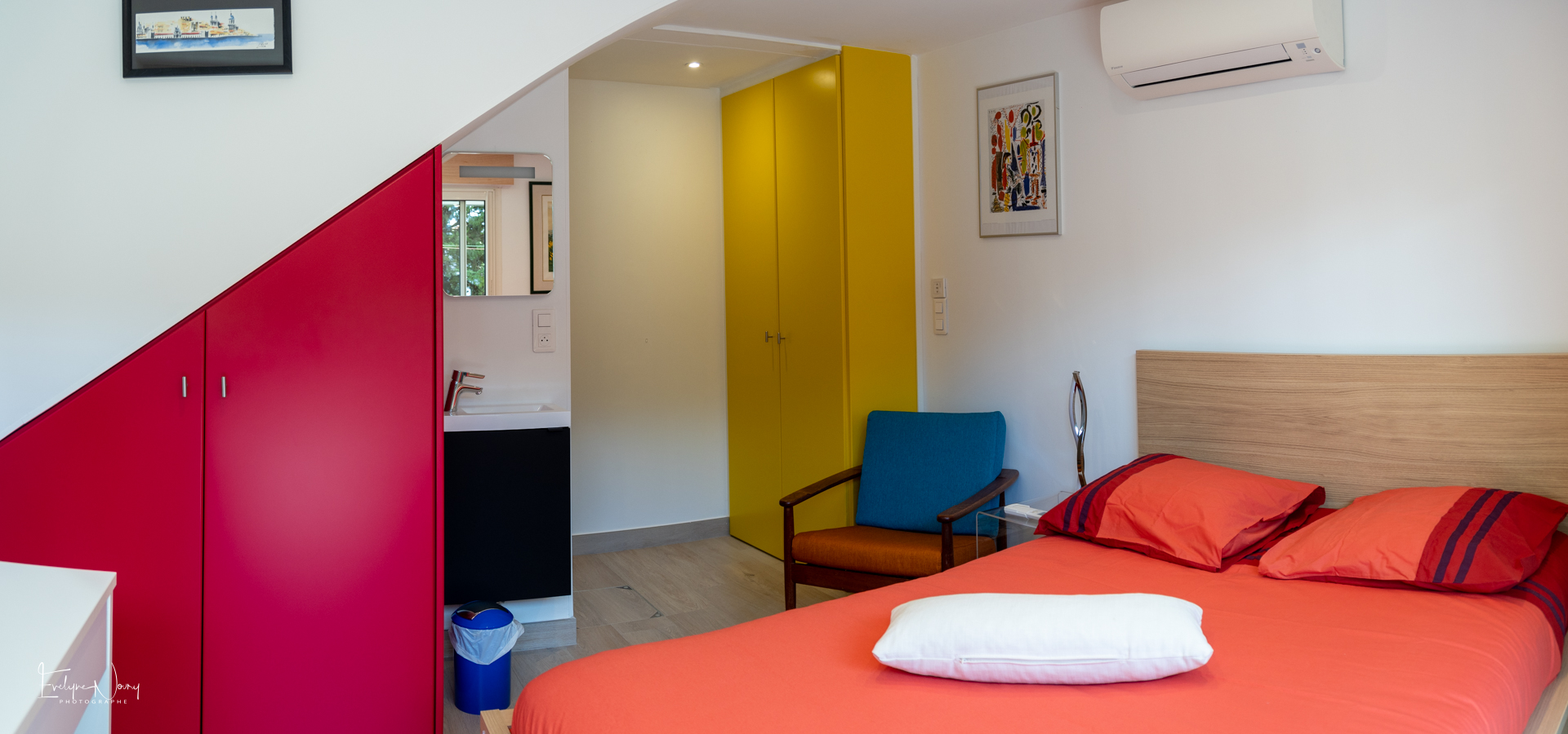 Minoury _ Chambre RDJ La Jardine 9 Panorama Chambre principale de l'appartement en rez-de-jardin. Lit 2 couchages, armoire, table, fauteuil, TV, lave-mains.